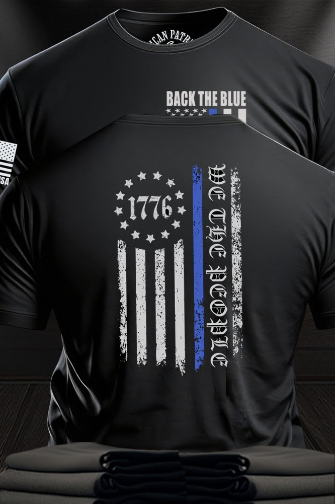 Patriot Gear USA Apparel Black t-shirt with text "Back the Blue" and a flag design with text "We the People", displayed against a wooden  American Outfitters Apparel Company background.