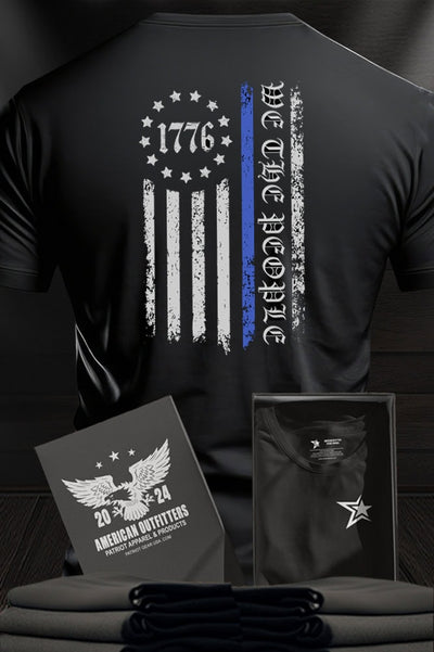 Patriot Gear USA Apparel Black t-shirt with text "Back the Blue" and a flag design with text "We the People", displayed against a wooden background.