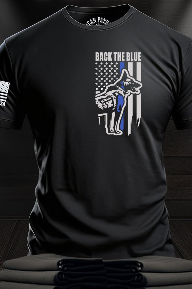 Patriot Gear USA Apparel Company Black t-shirt with a distressed American flag and K-9 dog design with text "Back The Blue" on a wooden surface.
