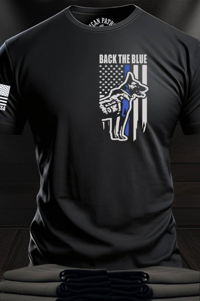 Patriot Gear USA Apparel Company Black t-shirt with a distressed American flag and K-9 dog design with text "Back The Blue" on a wooden surface.